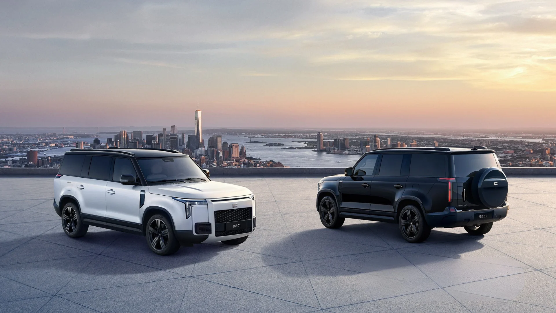 Two ROX 01 SUVs on a rooftop overlooking a city skyline at dusk